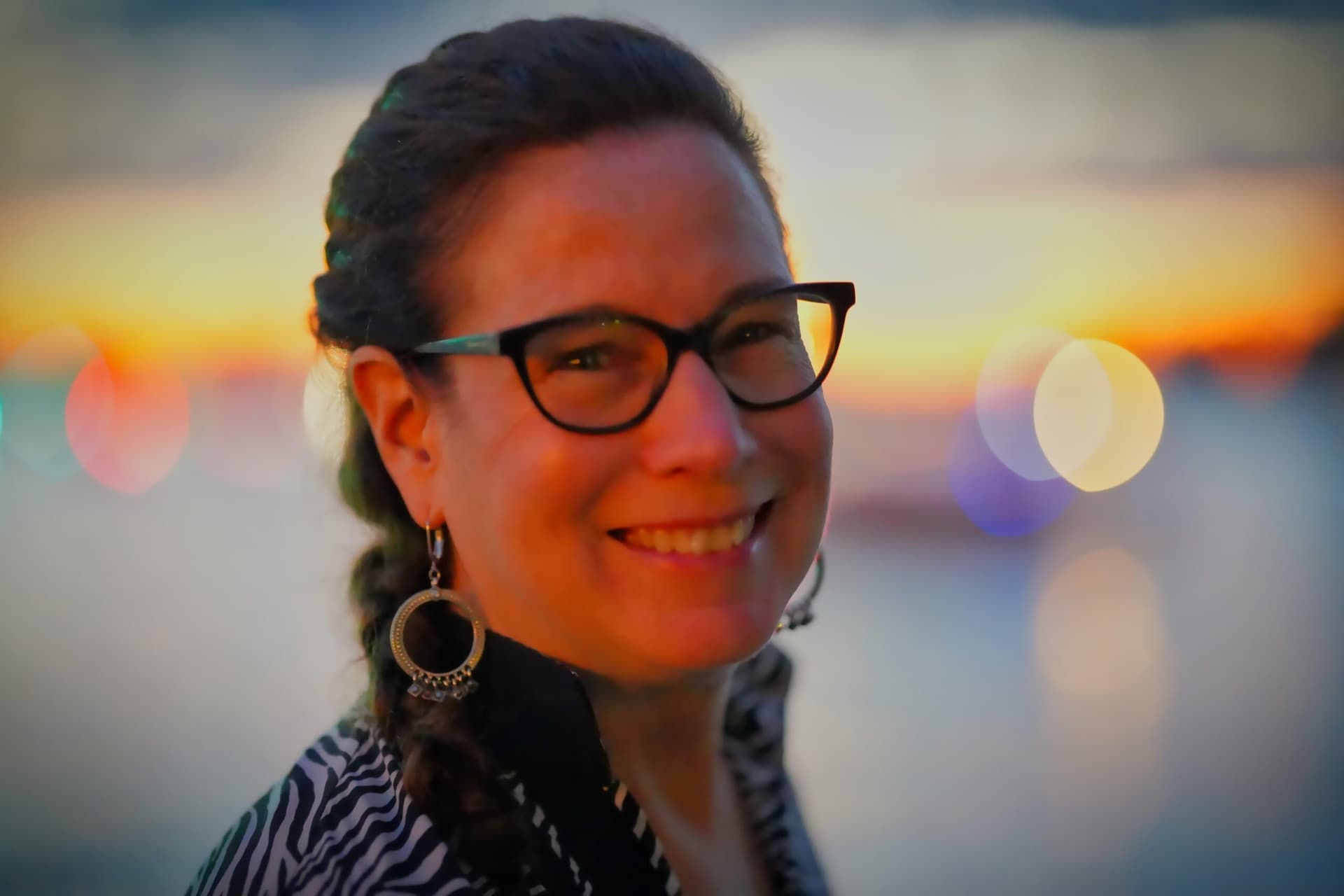 Portrait of a smiling woman at dusk with waterfront bokeh lights behind her